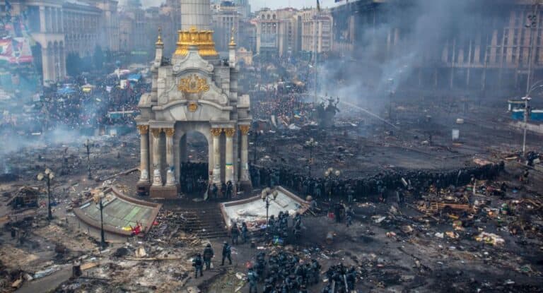 Ruined city square with damaged monument and chaos after conflict or disaster in urban setting.