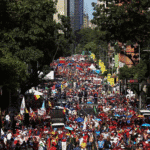 Endless crowded street protest with political flags, banners, and vibrant atmosphere in a busy city.