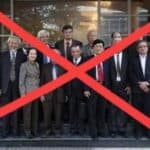 People in formal business attire standing outdoors, with a red X overlay.