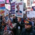Protest crowd holding signs against fascism and political figures in Times Square, New York City.