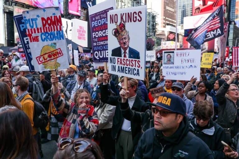 Protest crowd holding signs against fascism and political figures in Times Square, New York City.